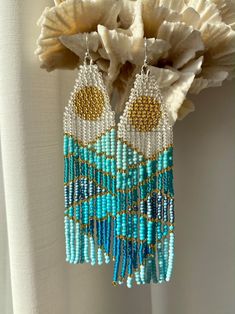 a pair of blue and white beaded earrings hanging from a coral flower with seashells in the background