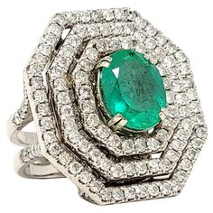 Ring size: 7 This incredible, jaw-dropping emerald and diamond cocktail ring is the absolute epitome of glamour. It features a single oval cut natural emerald in a stunning bluish-green color, double prong set at the center of the piece. A triple halo of icy white diamonds surround the center stone in a bold, octagonal shape, filling the finger from end to end with unbelievable sparkle. The white gold setting also really enhances the white brilliance of the diamonds. Set on a dome plate beneath the ring are additional pave diamonds, as well as along the top portion of the split shank, allowing the shimmering stones to be present from every angle. This is certainly a 'WOW' ring that will not go unnoticed! Ring size: 7 Weight: 22.4 grams Metal: 14 Karat White Gold Natural Diamonds: 5.81 ctw Luxury Fine Jewelry Green Halo Ring, Platinum Oval Emerald Ring With 17 Jewels, Oval Platinum Emerald Ring With 17 Jewels, Dazzling Oval Emerald Ring In Platinum, Diamond Cocktail Ring, White Gold Set, Diamond Jewelry Designs, Diamond Cocktail Rings, Bluish Green