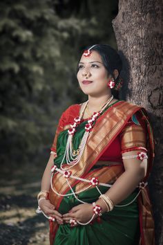 a woman in a green and red sari standing next to a tree with her hands on her hips