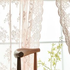 a wooden chair sitting in front of a window next to a vase with flowers on it