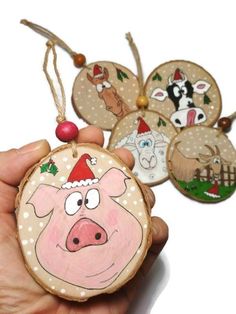 a hand is holding some ornaments with animals on them and one pig has a santa hat