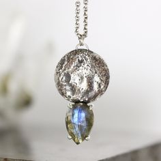 "A flashy blue rose cut pear labradorite hangs below a nature-inspired full moon casting in this pendant. The moon has been given a light patina to bring out its highlights and texture. The pendant measures 1\" and hangs from a lightly patina-ed 16\" chain.  Stone: 12mm x 8mm natural labradorite Metal: Solid sterling silver This pendant is ready to ship. To see all the Ready to Ship jewelry in my shop, click here: https://www.etsy.com/shop/SarahHoodJewelry/search?search_query=ready+to+ship&order Silver Labradorite Jewelry With Moon Charm, Labradorite Moon Phase Round Necklace, Round Labradorite Moon Phase Necklace, Labradorite Moon Phase Pendant Necklaces, Labradorite Moon Phase Pendant Necklace, Labradorite Moon Shaped Necklace With Moon Charm, Silver Moon-shaped Nature-inspired Jewelry, Labradorite Gemstone Teardrop Pendant Jewelry, Unique Labradorite Teardrop Pendant Jewelry