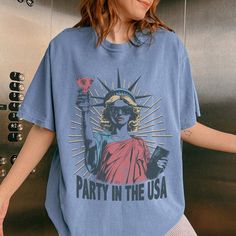 C O M F O R T    C O L O R S Get ready to be OBSESSED with your new 4th of July Statue of Liberty shirt. It's the cutest and most trendy way to emit all those important trendy vibes! This is the perfect  fourth of July shirt!  * Q U I C K * F A C T S * ✺  All shirts are UNISEX ✺  100% Airlume combed and ringspun cotton (fiber content may vary for different colors) ✺ Wash and dry normally (on cool for best results) * S I Z I N G * ✺ For an oversized fit, select two or three sizes up from your normal size ✺ Model is wearing size L  ✺ Sizing runs true to size ✺ Most women find their typical size works best, since they are meant to fit a touch loose ✺ Runs a little small for men so please size up for the best fit ✺ See Size guide and fit in images          * S H I P P I N G * T I M E S * ✺ Our Casual Blue T-shirt For Independence Day, Blue Short Sleeve T-shirt For Independence Day, Retro American Flag Print Summer T-shirt, Blue T-shirt With American Flag Print For Spring, Blue Crew Neck T-shirt For Labor Day, Relaxed Fit Letter Print Tops For 4th Of July, Graphic Tee For 4th Of July With Crew Neck, 4th Of July Graphic Tee With Crew Neck, 4th Of July Graphic Tee Shirt