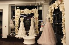 wedding dresses are on display in front of a window with flowers and ribbons hanging from it