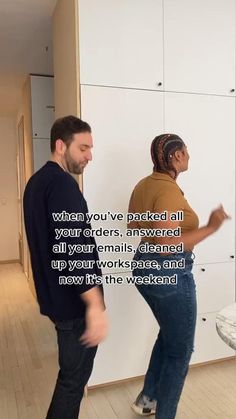 two people standing next to each other in a room with white cabinets and wood floors