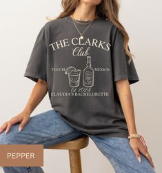 ABOUT OUR: Luxury Bachelorette Merch Comfort Colors The Comfort Colors 1717 shirt features a vibrant design capturing the essence of celebration in Tulum, Mexico. "The Clarks Club" boldly adorns the front, personalized for the occasion. A glass filled with a tantalizing drink sits at the center, flanked by custom tequila bottles, symbolizing the spirit of festivity. "EST. 2024" marks the year of the memorable gathering, while "Claudia's Bachelorette" adds a personal touch, commemorating a special milestone. This shirt embodies the joy, camaraderie, and adventure of unforgettable moments shared with loved ones. SIZING  ❥ TSHIRT has a unisex fit. Runs true to size. ❥ Please refer to size chart before ordering. If possible, measure your favorite t-shirt armpit to armpit and top to bottom and Luxury Festive Party Shirt, Drinking Bachelorette Shirts, Bachelorette Merch, Luxury Bachelorette, Wedding Social, Tequila Bottles, Bridal Party Shirts, Club T Shirt, Tulum Mexico