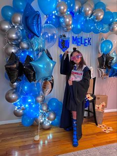 a woman standing in front of a balloon arch with blue and silver balloons on it