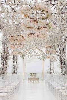 an outdoor ceremony setup with white chairs and pink flowers on the arbors at the end of the aisle