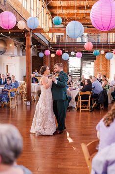 a bride and groom sharing their first dance at the wedding reception with paper lanterns hanging from the ceiling