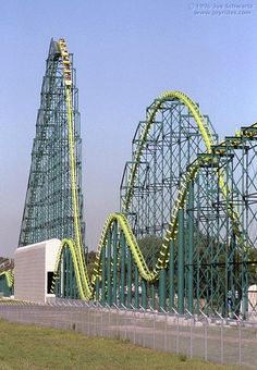 the roller coaster is green and has yellow trim on it's sides, as well as two other roller coasters