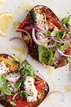 two open faced sandwiches with tomatoes, onions and herbs on them next to lemon wedges