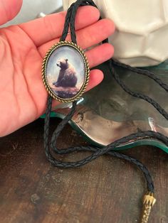 a hand holding a necklace with a picture of a bear in the center on it