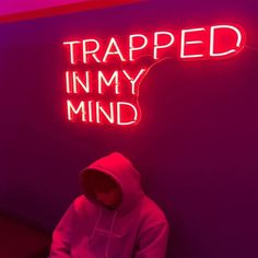 a person sitting in front of a neon sign that says trapped in my mind on the wall