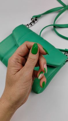 a woman's hand with green and white nail polish holding onto a green purse