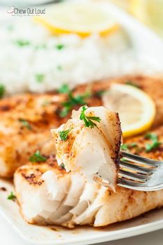 a piece of fish on a white plate with a fork in it and lemon wedges