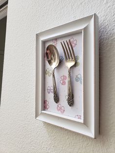 two forks and spoons are in a white frame with pink flowers on the wall