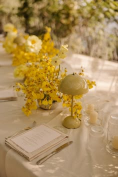 the table is set with yellow flowers and place settings for guests to sit down at