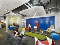 people are playing golf in an office setting with chairs and couches, while one man is on his laptop