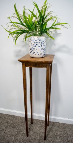 a small wooden table with a plant on top and a white vase sitting on it