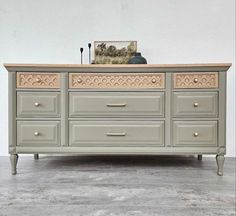 a dresser with drawers and an ornate design on the top, painted in light gray