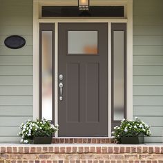 a gray front door with two planters on the steps and a light above it