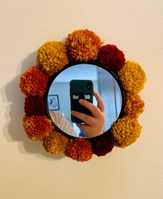 a person holding a cell phone in front of a mirror with pom - poms