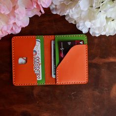 an orange leather wallet with two credit cards in it and flowers on the table next to it