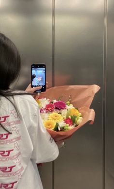 a woman taking a selfie with her cell phone while holding a bouquet of flowers