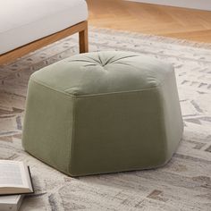 a small green ottoman sitting on top of a rug next to a chair and book