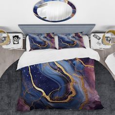 a bed with a blue and gold comforter next to a mirror on the wall