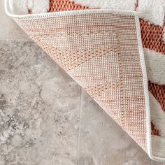 an orange and white rug on the floor next to a gray tile floor with a red and white pattern