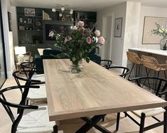 a dining room table with chairs and flowers in a vase on the top, next to an open kitchen area