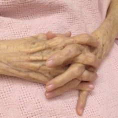 an old woman holding her hands on top of a pink towel