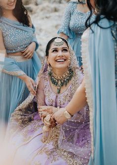 two women dressed in blue and one wearing a purple sari smiling at each other