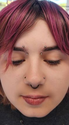 a close up of a person with pink hair and piercings on her nose wearing a black sweater