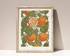 an orange print with green leaves on a white wall next to a wooden framed frame