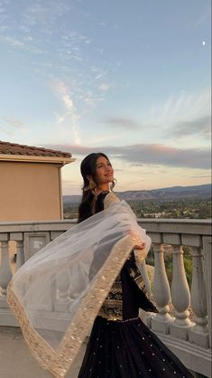 a woman is standing on a balcony with her veil blowing in the wind and looking up into the sky