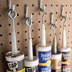 three toothbrushes and two cans of paint on a pegboard with hooks attached to it