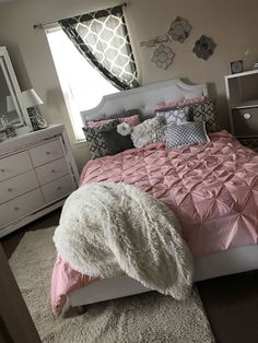 a bedroom with pink and gray bedding, white dressers and mirror on the wall