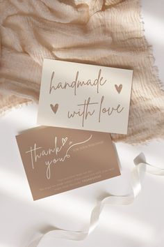 two thank cards sitting on top of a white blanket next to a brown and white ribbon