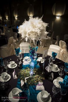 the table is set with blue and white dishes, silverware, and feathers in a vase