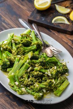 a white plate topped with broccoli on top of a wooden table next to lemon wedges