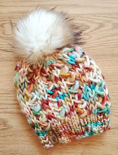 a multicolored knitted beanie with a white fur pom