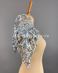 a mannequin's head is adorned with intricate silver metalwork and a wooden stick