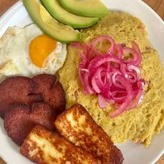 a white plate topped with eggs, hash browns and avocado next to sliced red onions