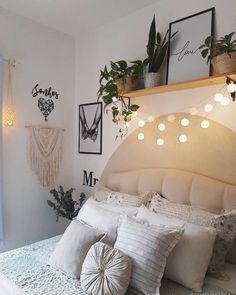 a white bed topped with lots of pillows next to a wall filled with pictures and plants