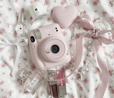 a pink camera sitting on top of a bed next to perfume bottles and a bow