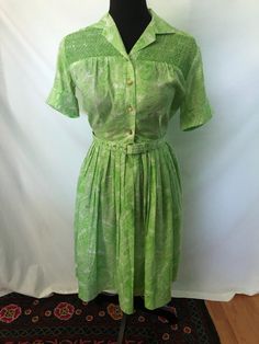 1950s Flutterbye green paisley shirtwaist dress with smocked yoke: This cotton collared and belted dress bass shirt roll-up sleeves. It features machine made smocking at the yoke. It has center front button and snap closure. Measurements: Bust 36 in. Waist 26 in. Length 38 in. Green Retro Vintage Dress, Retro Green Dress With Vintage Print, Vintage Smocked Fitted Dress, Fitted Smock Vintage Dress, Vintage Smock Dress For Daywear, Fitted Vintage Smock Dress, Fitted Green Vintage Dress, Green Vintage Style Dress For Summer, Green Vintage Dress For Summer