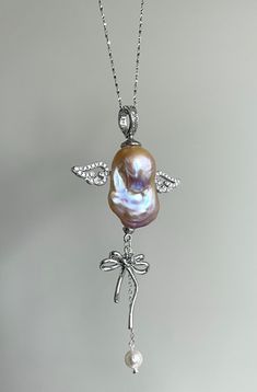 Elevate your elegance with this exquisite necklace that features a unique pendant designed to resemble an angel, featuring a lustrous baroque pearl. This stunning blend of natural beauty and exquisite craftsmanship floats with two sparkling silver wings, with a dangling bow and round pearl, providing a harmonious balance to the overall design. Whether you are looking for an unique element to your evening attire or a fresh look to your everyday jewellery, this piece is a perfect addition to your Silver Baroque Pearl Necklace Gift, Silver Baroque Necklace With Pearl Pendant, Baroque Silver Necklace With Pearl Pendant, Silver Baroque Necklace With Pearl Charm, Sterling Silver Baroque Jewelry For Gifts, Baroque Pearl Pendant, Everyday Jewellery, Silver Wings, Pearl Charms