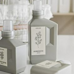 a bottle of liquid sitting on top of a white table next to a container with flowers